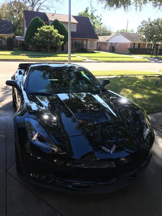 A black Corvette Stingray freshly detailed on a residential driveway in front of a brick ranch style house